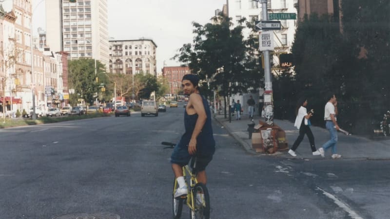 A young Shawn Regruto on a yellow bicycle in the middle of a New York City street, looking back over his shoulder.