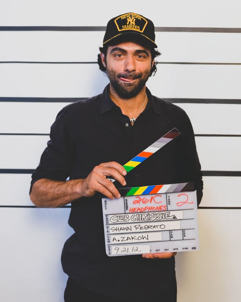 Shawn Regruto in a Yankees cap, holding a film slate that names him as director, in front of a height chart.
