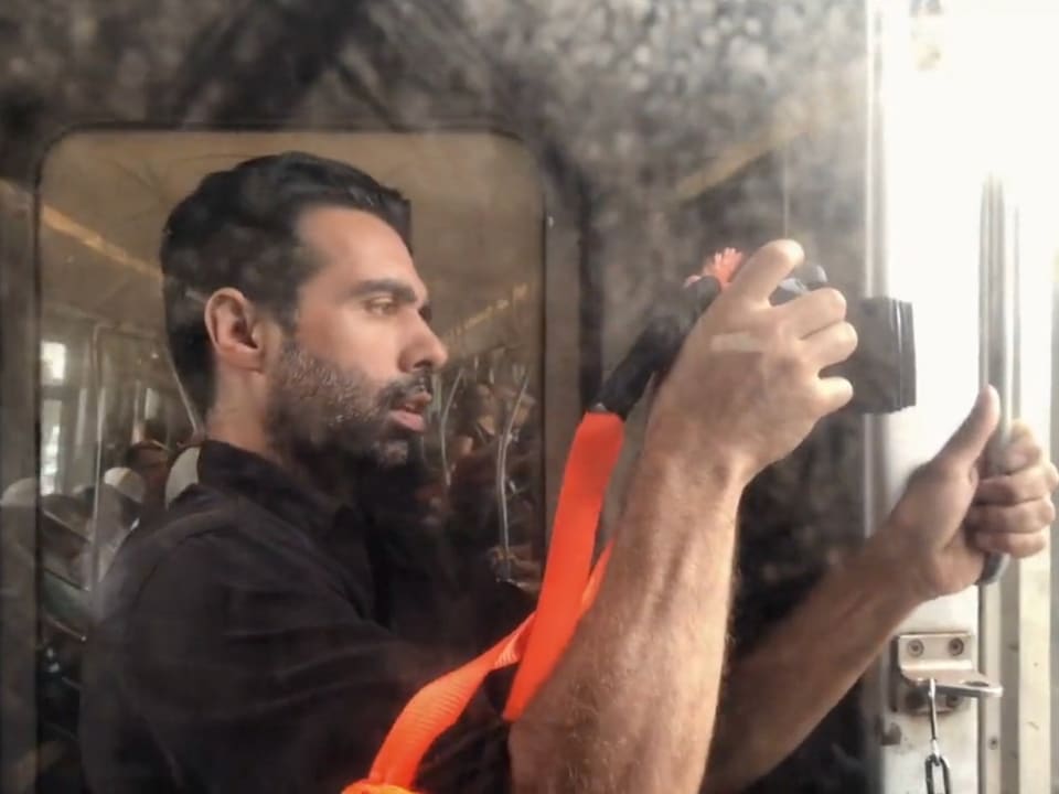 Shawn Regruto in profile, holding a small camera up to a bright window.